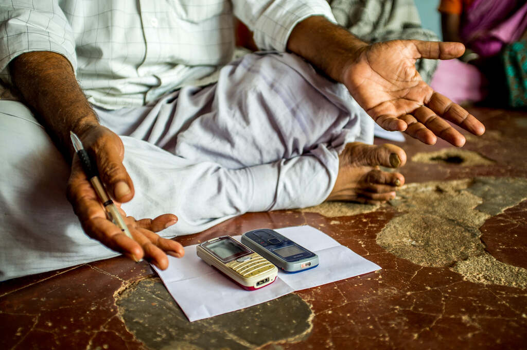 A man sits crosslegged before two old cellphones-digital divide in India